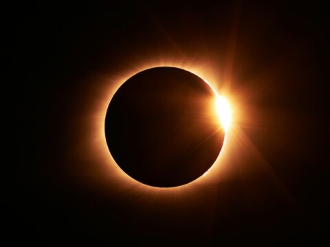 Image of a near total solar eclipse. A black circle (the moon) is backlit with a ring of light (the sun) against a black background.