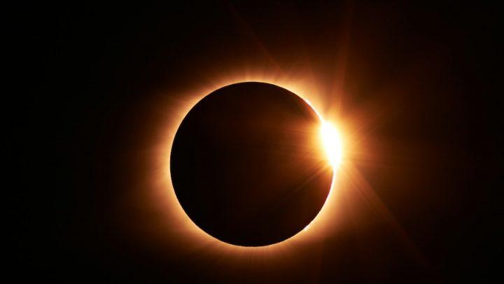 Image of a near total solar eclipse. A black circle (the moon) is backlit with a ring of light (the sun) against a black background.