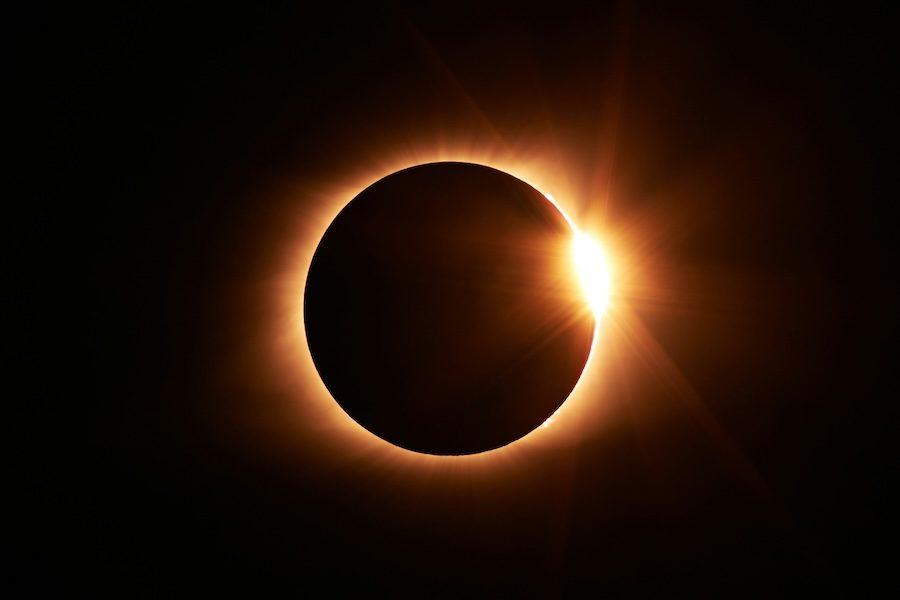 Image of a near total solar eclipse. A black circle (the moon) is backlit with a ring of light (the sun) against a black background.