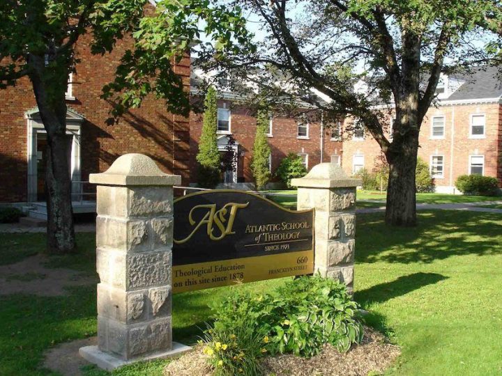 A sign reading "Atlantic School of Theology" sits on the grass, in front of brick buildings.