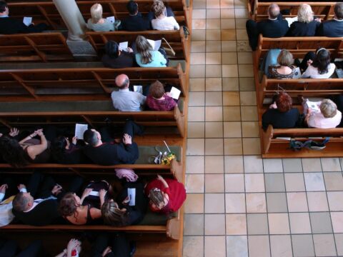 Aerial view of a church congregation. The floor has different coloured tiles, you can see the church pews are filled with people and the tops of their heads.