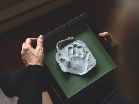 A child's handprint in the centre of a green box. The hands of an adult woman are visible, holding the box.