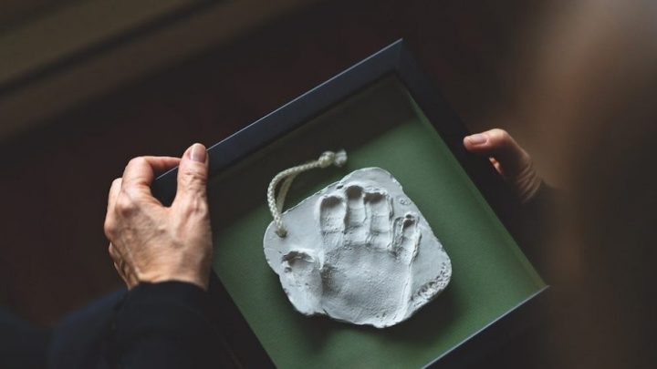 A child's handprint in the centre of a green box. The hands of an adult woman are visible, holding the box.