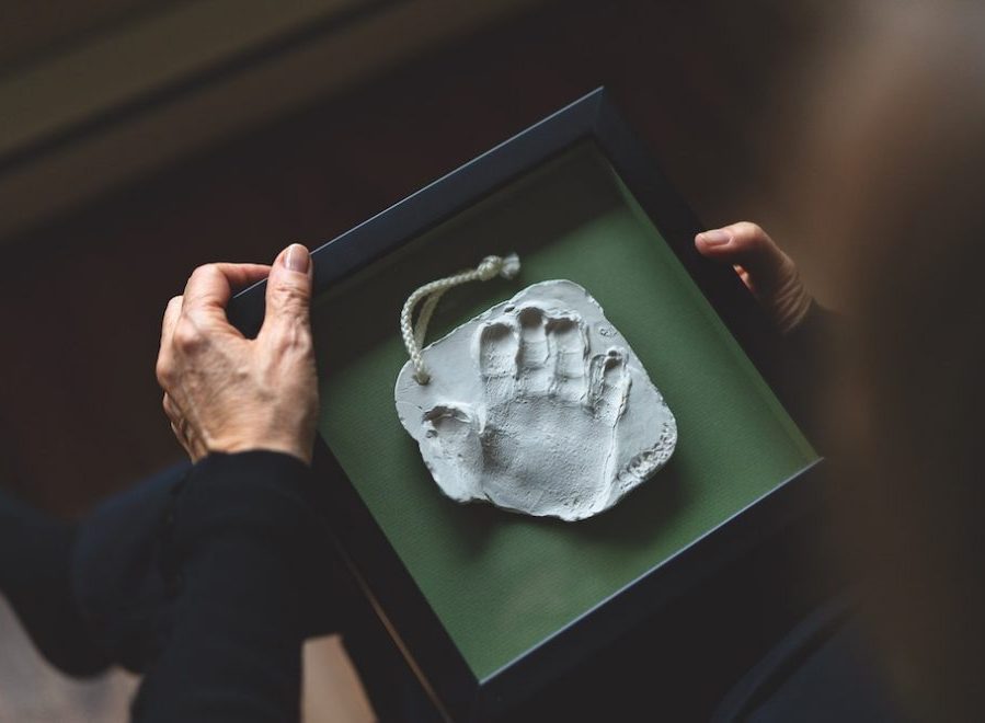 A child's handprint in the centre of a green box. The hands of an adult woman are visible, holding the box.