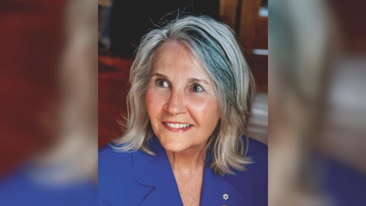 Headshot of a middle-aged white woman with shoulder-length grey hair. She is smiling and wearing a blue blazer.