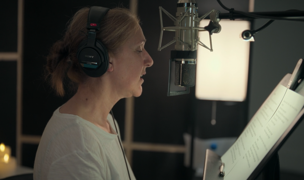 Side profile of Celine Dion, who is facing a microphone and wearing headphones. In front of her seems to be a music stand with sheet music.