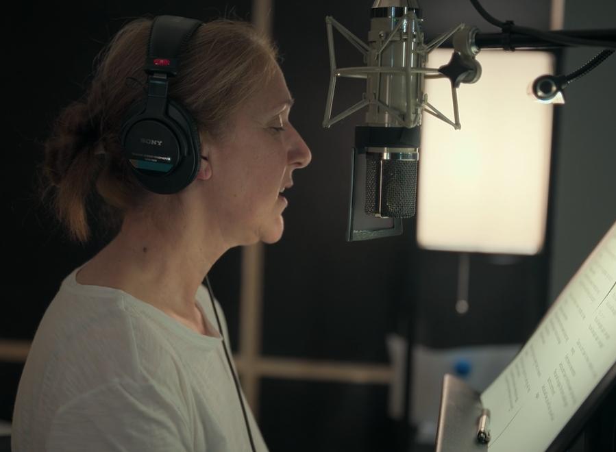 Side profile of Celine Dion, who is facing a microphone and wearing headphones. In front of her seems to be a music stand with sheet music.