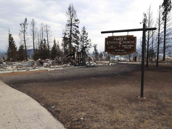 A sign reading "Jasper United Church" sits at the foreground of the image. Behind it, there is debris from the fire.