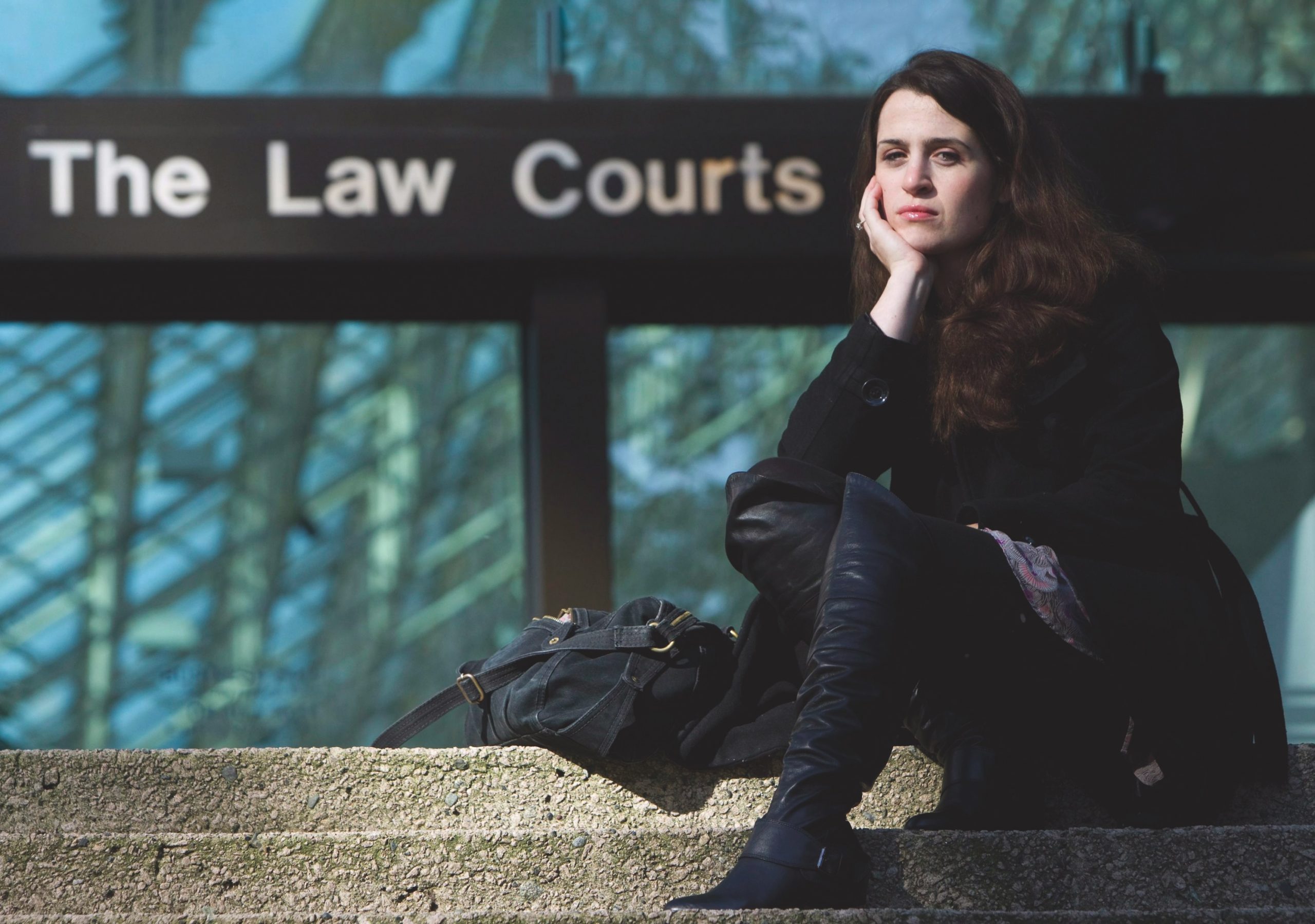 Olivia Pratten poses on the steps of a court of law, seated, dressed in all black.