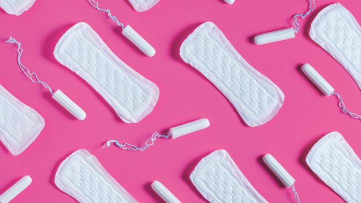 Image of period products with white tampons and pads laid out on a pink background