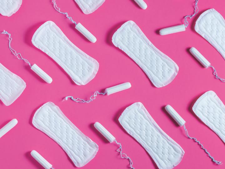 Image of period products with white tampons and pads laid out on a pink background