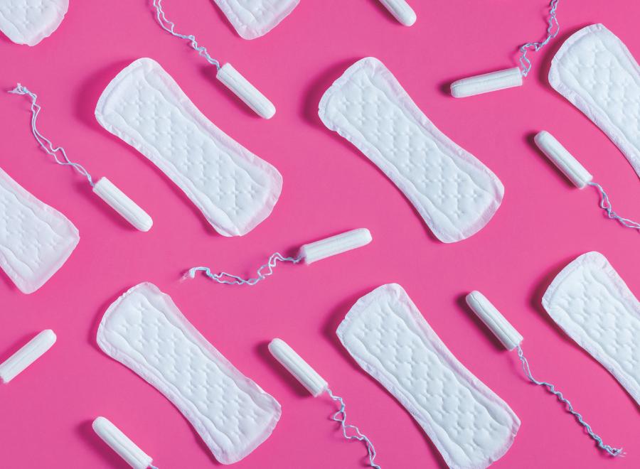 Image of period products with white tampons and pads laid out on a pink background