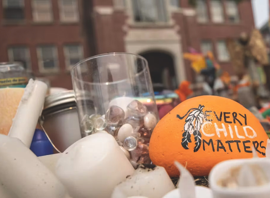 A glass holding rocks is next to a rock that is painted orange. It has a dreamcatcher on it and the words, "Every child matters". 