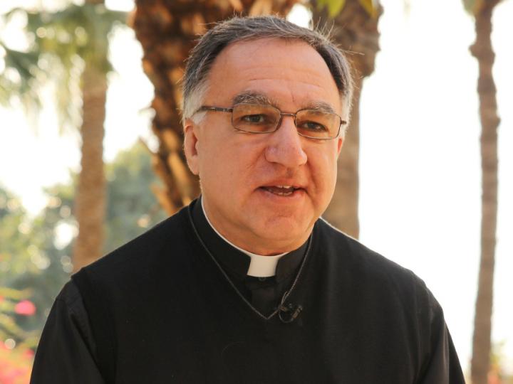 A man dressed in a black shirt with a priest's collar. He wears glasses.