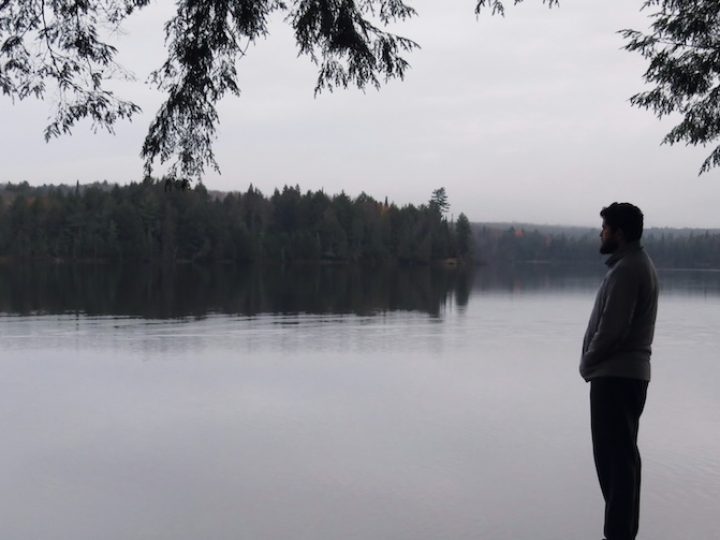 Black and white photo of a man standing by a lake. It is a side profile of the man.