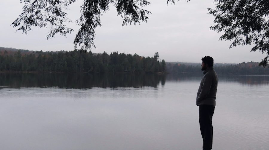 Black and white photo of a man standing by a lake. It is a side profile of the man.