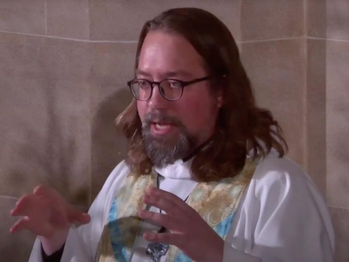 A Screenshot from a YouTube video shows a man with glasses and preacher's robes standing and talking.