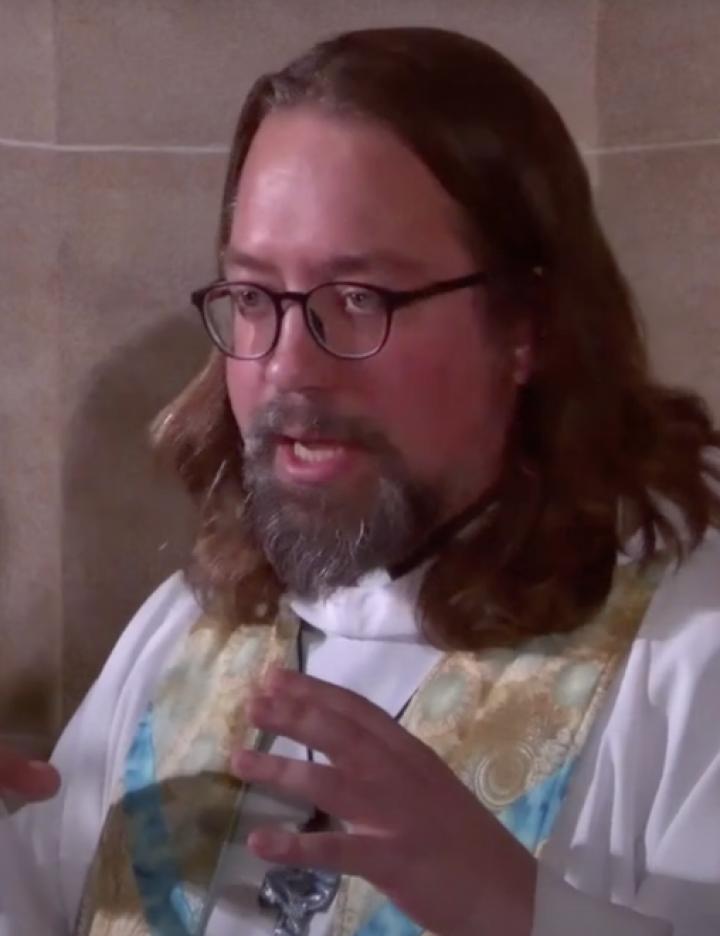 A Screenshot from a YouTube video shows a man with glasses and preacher's robes standing and talking.