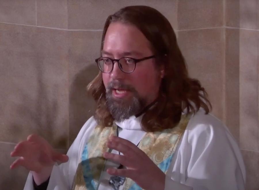 A Screenshot from a YouTube video shows a man with glasses and preacher's robes standing and talking.