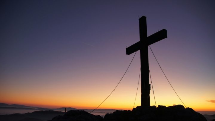 A cross stands against a dusk backdrop. The sun is setting and the sky is dark.