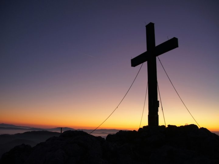 A cross stands against a dusk backdrop. The sun is setting and the sky is dark.