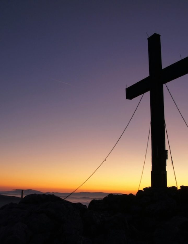 A cross stands against a dusk backdrop. The sun is setting and the sky is dark.