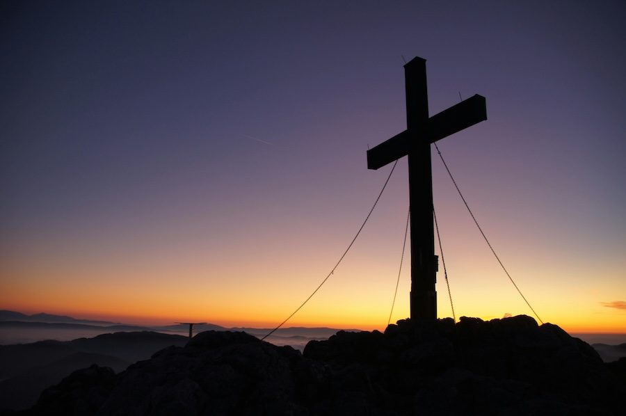 A cross stands against a dusk backdrop. The sun is setting and the sky is dark.