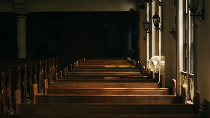 A photo of a row of pews in a darkly-lit church.