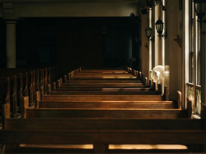 A photo of a row of pews in a darkly-lit church.