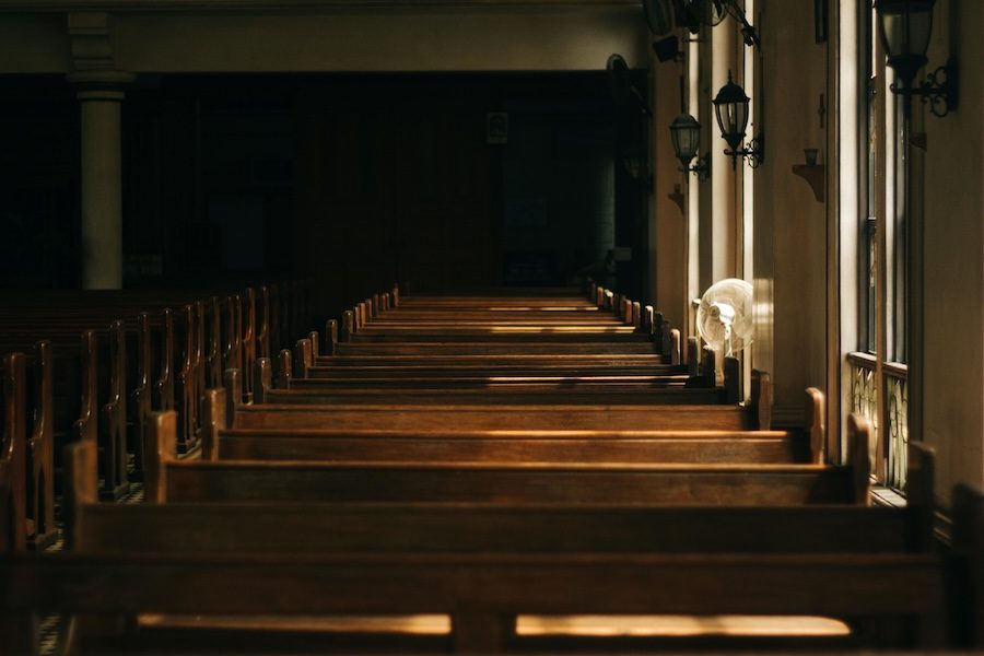 A photo of a row of pews in a darkly-lit church.