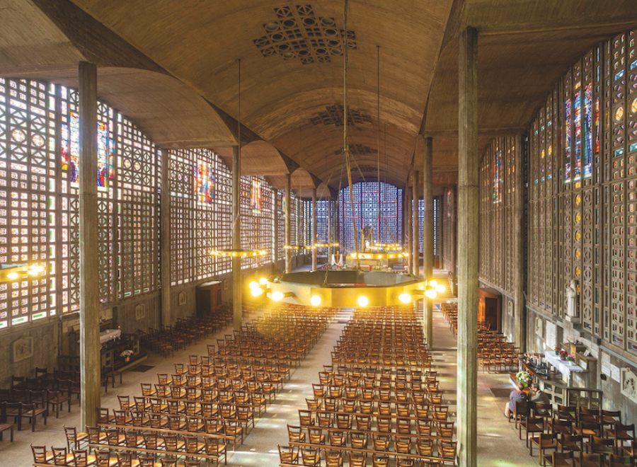 Interior of a church where the pulpit is lit up, there are rows of chairs and light streams in through the stain glass windows