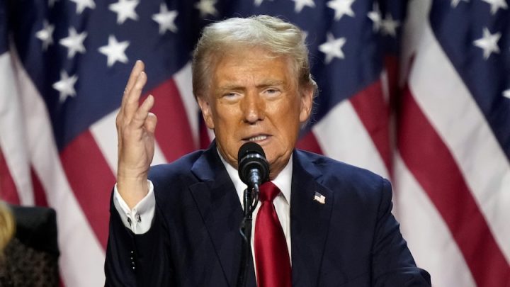 U.S. President Donald Trump speaks with his right hand up and in front of an American flag