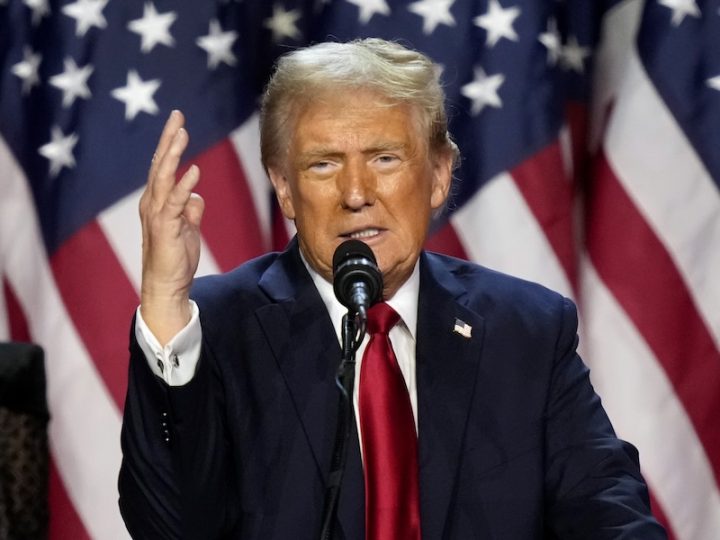 U.S. President Donald Trump speaks with his right hand up and in front of an American flag