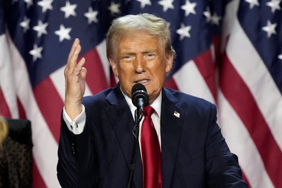 U.S. President Donald Trump speaks with his right hand up and in front of an American flag