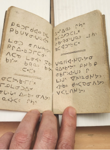 An open book of Cree syllabic writing in an open page with a person's hands holding it open