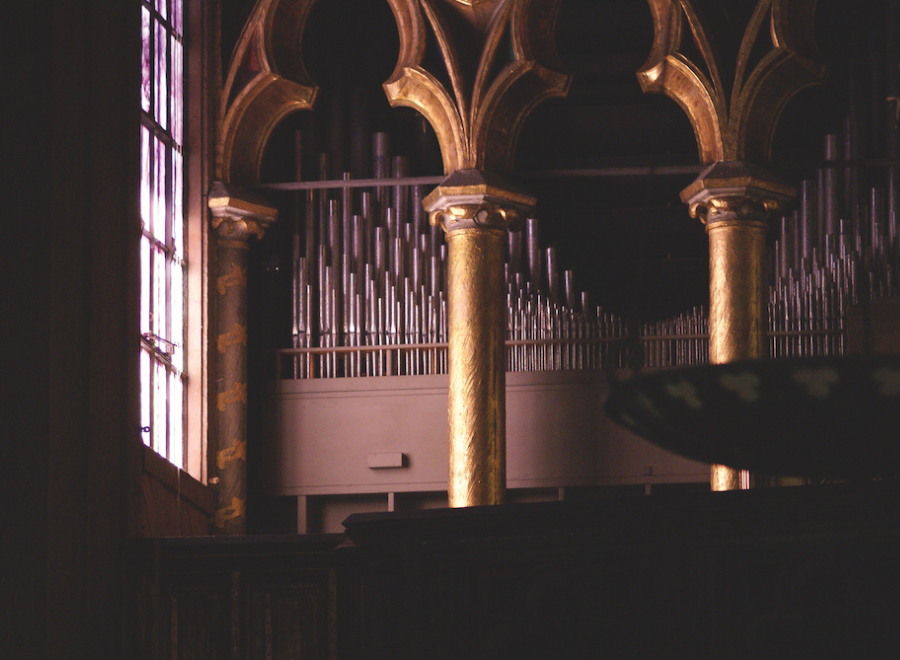 Inside of a church with a window and top of an organ in focus