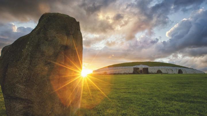 A backlit image of the sun shining along the horizon. A rock stands in front of it.