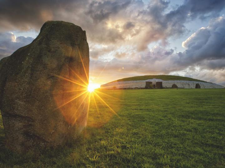 A backlit image of the sun shining along the horizon. A rock stands in front of it.