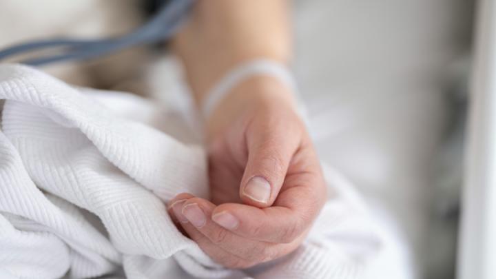 A white person's land is on a bed. They have a hospital bracelet on.