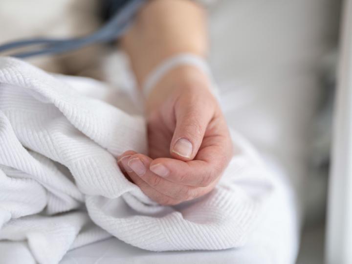 A white person's land is on a bed. They have a hospital bracelet on.