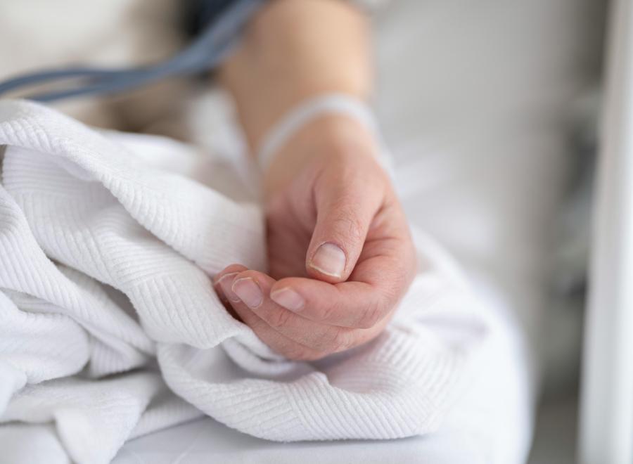 A white person's land is on a bed. They have a hospital bracelet on.