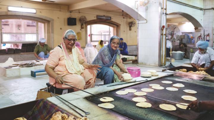 Two brown skinned women sit in front of a hearth where they are making chapatis in Delhi.