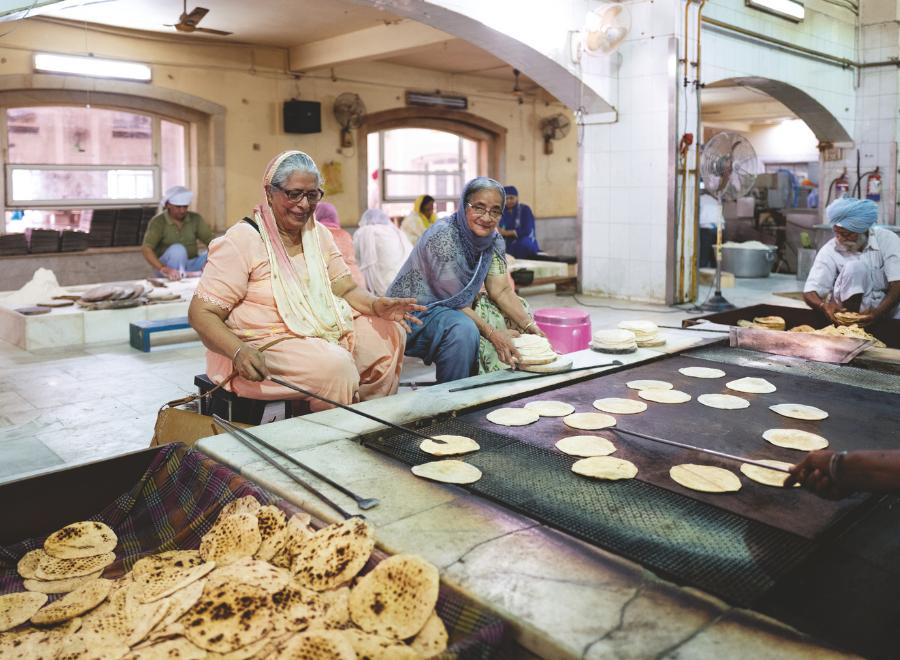 Two brown skinned women sit in front of a hearth where they are making chapatis in Delhi.