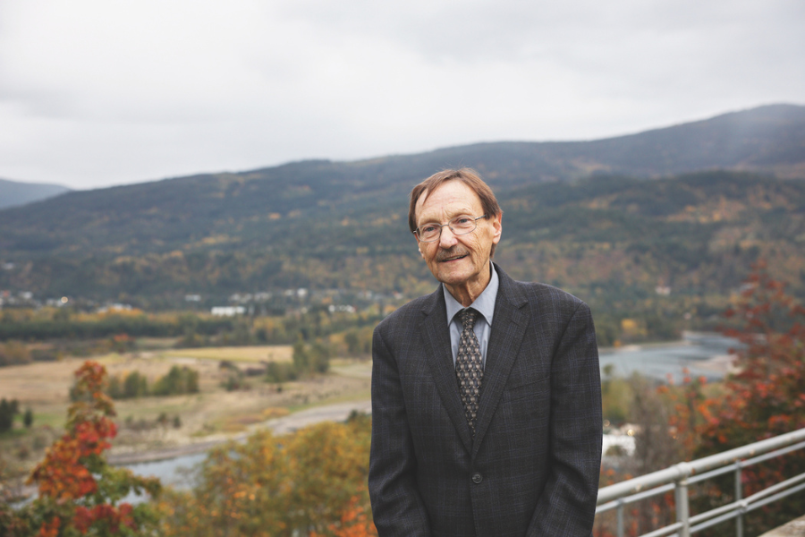 An older white man with brown hair and glasses is wearing a black suit and tie