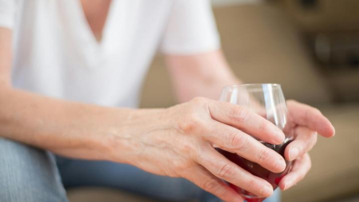 A white man in a white t-shirt holds a glass or red wine