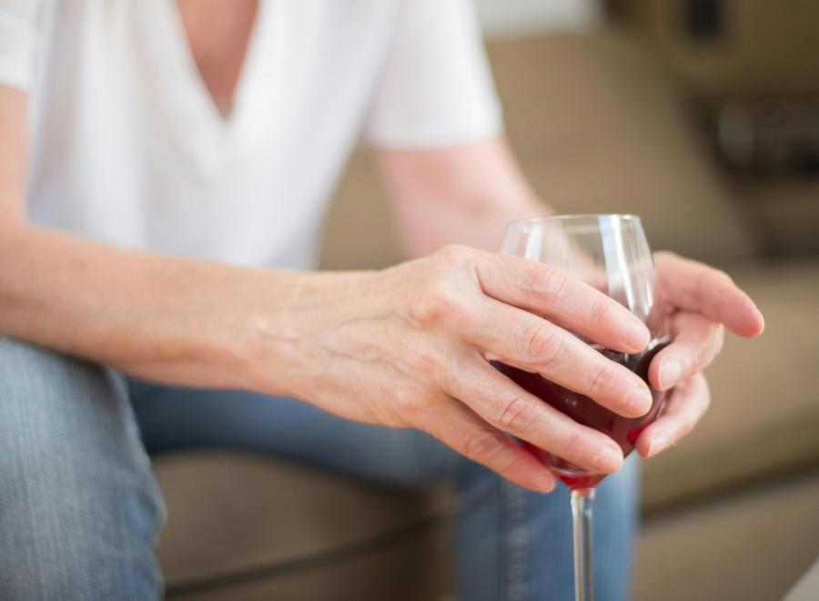 A white man in a white t-shirt holds a glass or red wine