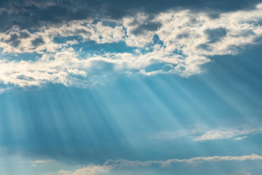 Rays of sunshine shine through clouds and a blue sky