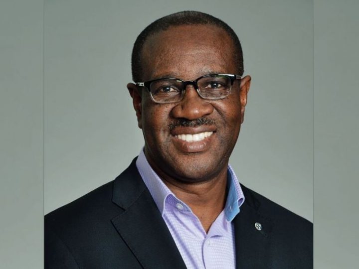 A smiling man in a suit and glasses against a neutral background.