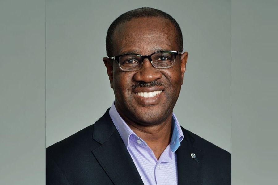 A smiling man in a suit and glasses against a neutral background.