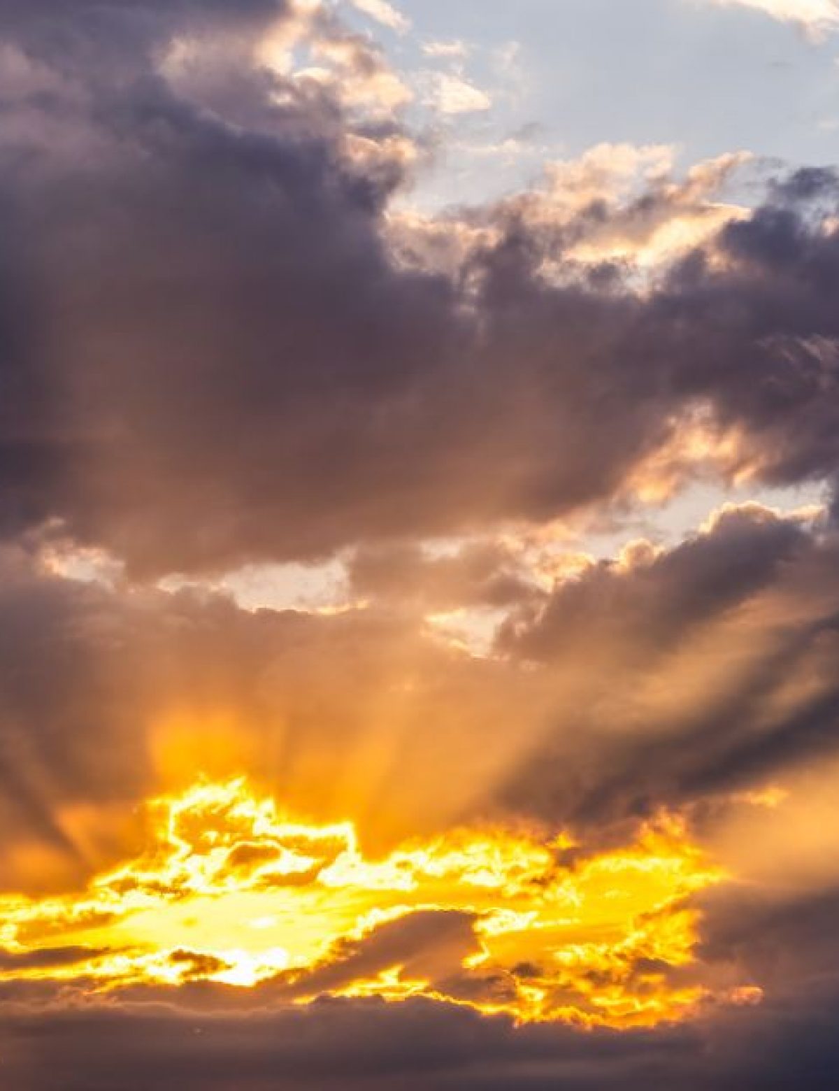 Dramatic golden rays of sunlight breaking through dark clouds, casting a warm glow across the sky at sunrise or sunset